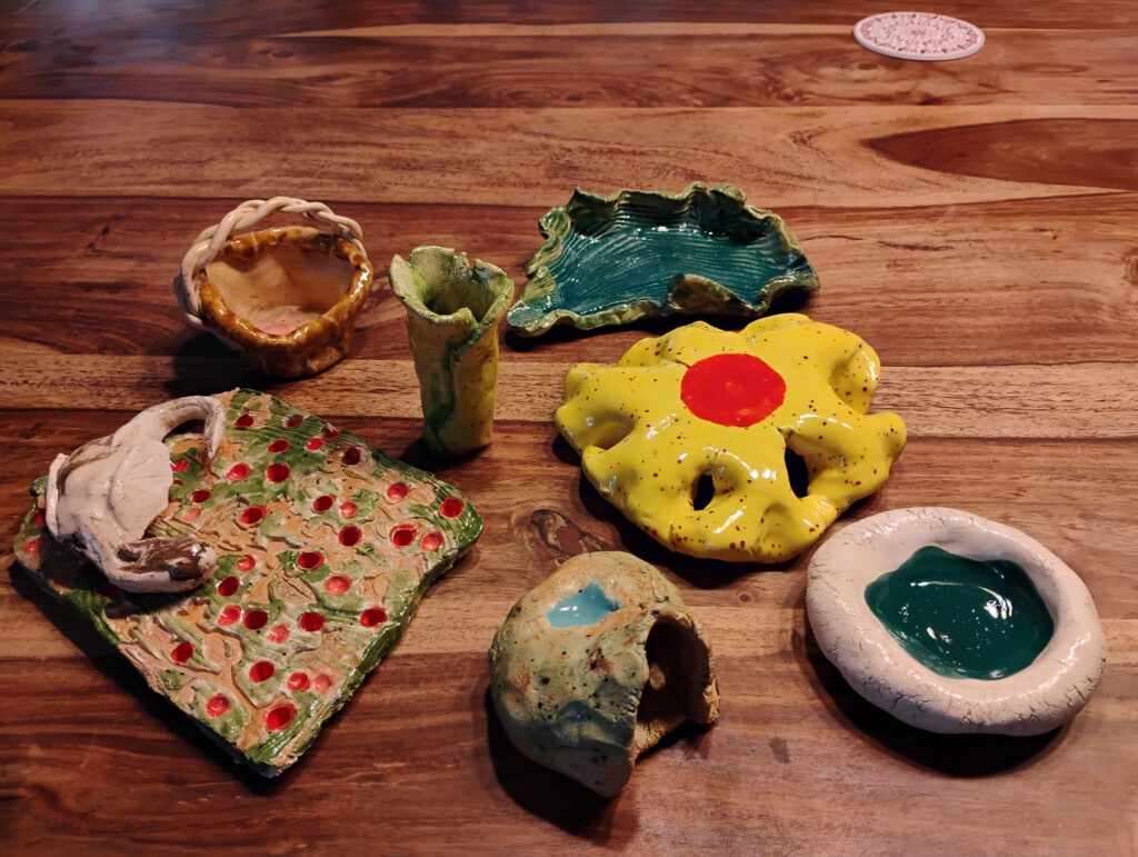 Diverse bunte, von Kindern getöpferte Gegenstände liegen auf einer Holzplatte
